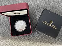 Photo of the silver coin in its burgundy display box next to the Royal Canadian Mint outer box, showing front side of coin with detailed design.