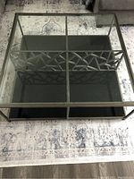 Overhead shot showing the square coffee table with a clear glass top and metal frame with geometric pattern inside base.