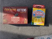 Photo shows two card game boxes side by side: Exploding Kittens Original Edition on the left and Family Charades on the right.