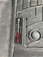 Close-up of WeatherTech brand label on molded black rubber floor mat.