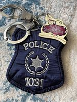 Navy blue fabric handbag with silver "POLICE 1031" embroidery and attached metal toy handcuffs, key tag from Bag Boutique visible