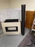 Full view of propane fireplace with two attached black vent pipes beside it on gray floor against wall.