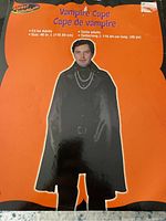 Front packaging of a black vampire cape for adults showing a model wearing it, labeled Planet Halloween brand, 46 inches long.