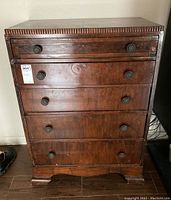 Front view of antique wooden chest of drawers showing five drawers with round metal knobs and scratched wood surface.