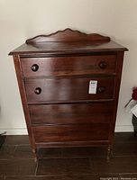 Front view of the antique wooden cabinet showing all four drawers and scalloped backboard on top.