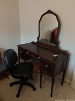 Front and side views of the antique vanity with attached arched mirror and clear knobs on drawers, alongside black office chair on wheels.