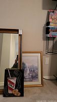Mirror with wooden frame next to two framed art pieces on the floor