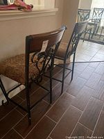 Two metal and wood bar stools with decorative backrest and patterned cushions shown from side angle on floor.