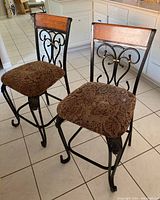 Two barstools with iron frames, wooden backrests, and paisley upholstered seats shown from a front angle.