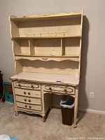 Full front view of a cream-colored vintage French provincial style bookcase desk combination with three shelves above and drawers below.