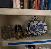 Shelf displaying metal bookend, frog bookends, and blue floral platter on stand alongside books
