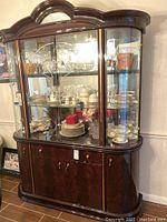 Front view of the dark wood china hutch showing upper glass display with etched glass and mirrored back, stocked with glassware and china, and lower storage cabinet.