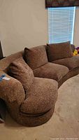 Curved sofa upholstered in brown and black tweed-like fabric with cushioned armrest and backrest.