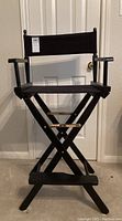 Full front view of the black director's chair showing the wooden frame, fabric seat, backrest, and armrests in a folded position.