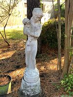Full view of garden statue standing by tree outdoors on pine needle ground