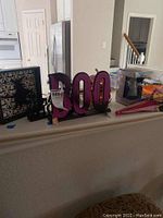 Photo of Halloween and Christmas decorations including a purple glittery 'Boo' sign and a framed shadow art with bat silhouette