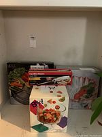 Photo showing the boxed Mikasa pink bowl, Hamilton Beach cutter, and Diamond Fire relish tray packages on shelf.