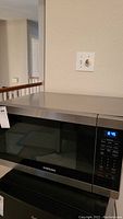 Front view of Samsung microwave showing stainless steel finish, glass door, and digital clock display active at 8:45.