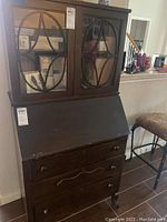Front view of wooden secretary desk with glass door cabinet and three drawers, showing scratches and wear.