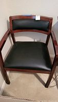 Front and angled view of one wooden side chair showing the black upholstered seat and backrest.