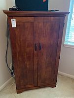 Front view of medium-brown wood cabinet with double doors and black handles. Scratches visible on surface.