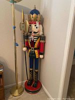 Full view of wood nutcracker statue next to brass-tone floor lamp