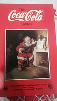 Red book cover titled 'The Coca-Cola Santas' with image of Santa Claus by the fireplace.