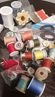 Photo of assorted sewing thread spools, scissors, needles, fabric patch, buttons, and other sewing accessories on a table.