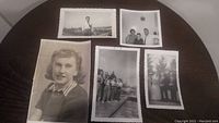 Lot of five vintage black and white photos on a round table, showing a mix of portrait and group shots