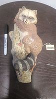 Photo showing top view of vintage Bossons raccoon figurine holding onto a tree trunk, includes a black permanent marker for size reference, measuring about 12.5 inches long. The raccoon is hand-painted with realistic details and has the original Bossons tag visible.