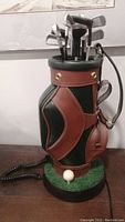 Full view of the golf club bag telephone showing the multiple golf clubs sticking out of the top of the bag and the base with golf ball detail