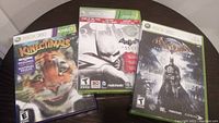 Three Xbox 360 game cases shown on round table featuring Batman: Arkham Asylum, Batman: Arkham City, and Kinectimals