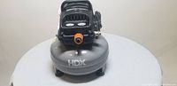 Front view of HDX portable air compressor showing pressure gauges, orange valve, and cylindrical tank.