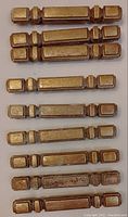 Top view of nine vintage brass cabinet pulls of varied lengths and styles: some solid bar style, others with mounting brackets, showing geometric stepped end design and patina.