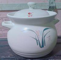 Side view of white ceramic cooking pot with orchid pattern and two handles.