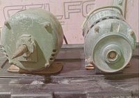 Side view of two electric motors placed on a black surface, showing conical shaft on one and pulley on the other.