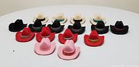 16 cowboy hat-shaped boxes in black, white, red, and pink arranged on table, empty or with necklaces inside.
