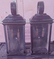 Front view of the two matching wrought iron wall sconces with glass panels. Shows design and condition of frames and bulbs inside.