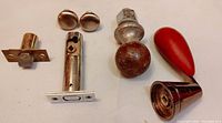 Photo showing assortment of vintage knobs and handles: door latch bolt, round wooden and metal doorknob, red bakelite handle, metal cabinet pull.