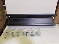 Black steel behind TV shelf laid flat with multiple labeled bags of screws and hardware in front.