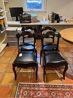 Four wooden chairs with faux leather seats arranged in a room with tiled floor and a window in the background.