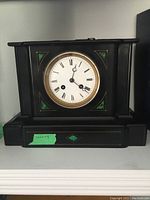 Front view of black wood mantel clock with green inlays and Roman numeral dial.