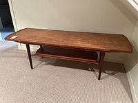 Front view of rectangular wood coffee table with tapered legs and lower shelf on carpeted floor