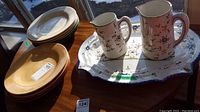Ten plates in five different colors stacked and shown next to the decorative platter and two matching jugs.