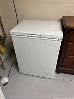 Front and side angled view of the white Frigidaire chest freezer closed, showing control dial and brand logo.