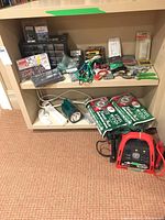 Wide view of beige shelving unit with assorted hardware items arranged on two shelves: plastic organizer with screws, ratchet socket set, flashlight, power strip, jumper cables, and packs of screws