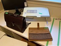 Photo showing the laptop stand with cooling fan, leather briefcase, and padded laptop case on a desk.
