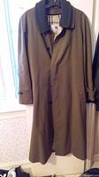 Full front view of olive green Burberry trench coat hung on hanger