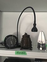 Full shelf view showing hygrometer, lamp, metronome, and decorative container on a shelf