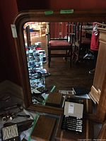 Front view of the large wood framed mirror reflecting various items in the room, showing the mirror's rectangular shape and rounded top corners.